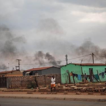 A man walks in front of a buildings, with smoke rising in the background