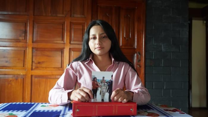 A woman holding a picture of a young girl looks to camera