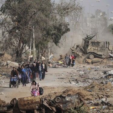 Families walk along a road with their possessions while smoke billows behind them