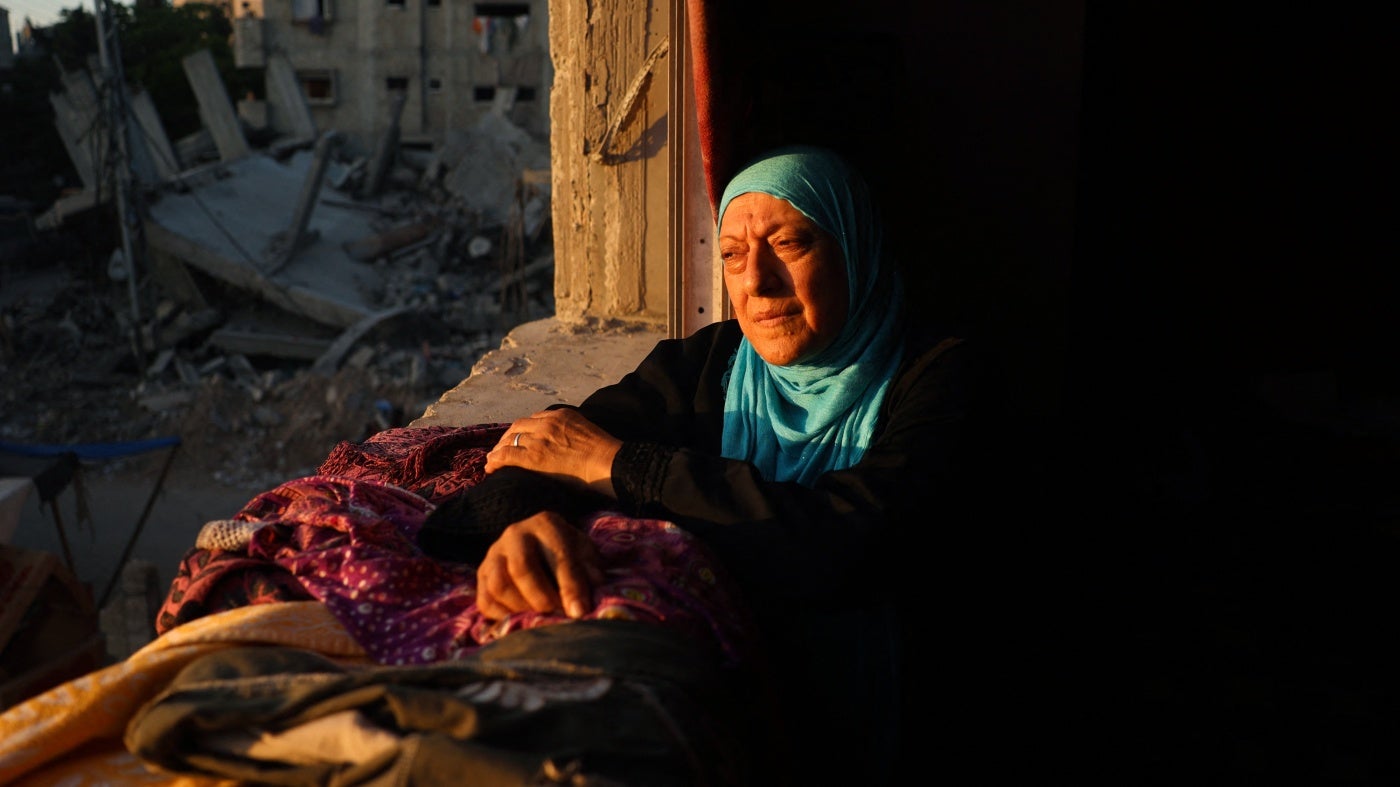 A woman looks out of the window of a damaged building