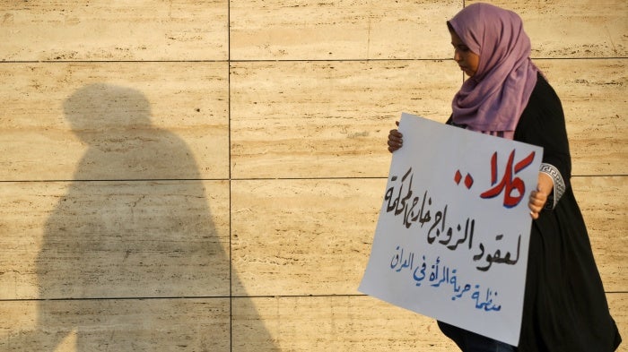 A woman walks holding a placard as activists demonstrate against female child marriages, in Tahrir Square, central Baghdad, July 28, 2024. 