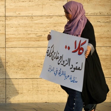 A woman walks holding a placard as activists demonstrate against female child marriages, in Tahrir Square, central Baghdad, July 28, 2024. 