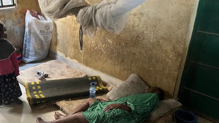 Aisha stands by her mother, lying on a worn-out and dirty mattress.