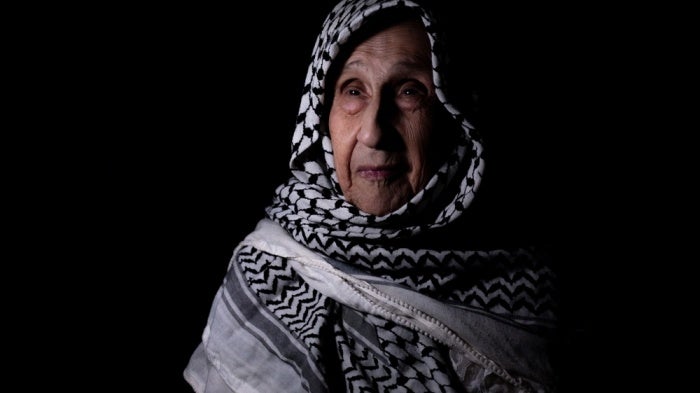 A photo of an older woman wearing a keffiyeh as a headscarf.