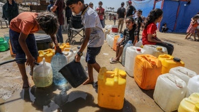 Palestinians wait to receive clean drinking water distributed by aid organizations in Deir al-Balah, Gaza, June 10, 2024.