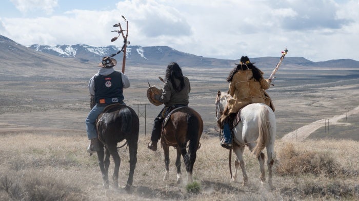 Three men sit atop horses overlooking a valley 