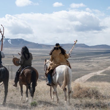 Three men sit atop horses overlooking a valley 