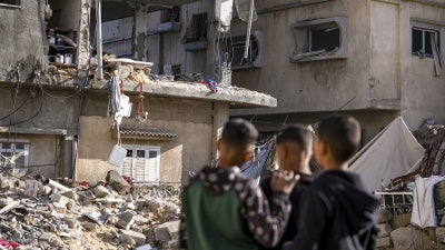 Three men look at a damaged building destroyed from an Israeli strike.